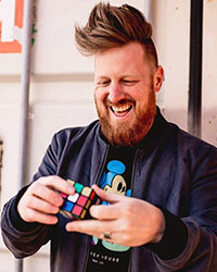 John Michael Hinton is smiling while solving a Rubik's Cube.