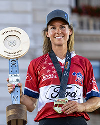 Martha King standing on a podium, holding a trophy and wearing a medal from a world championship jumberjill competition.