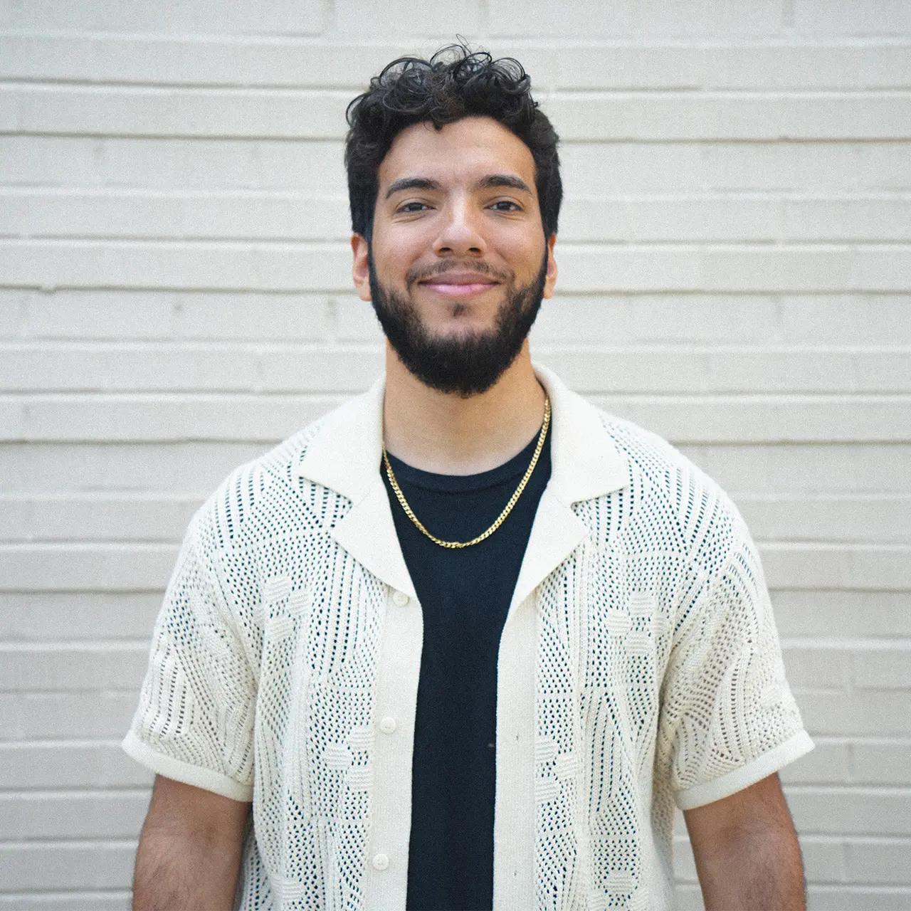 Christian DeLaCuba is smiling and wearing a black shirt with a white shirt on top.
